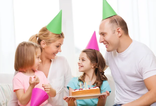 Lachende gezin met twee kinderen in hoeden met cake — Stockfoto