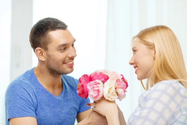 Uomo sorridente dando girfriens fiori a casa — Foto Stock