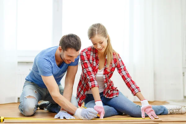 Coppia sorridente misurazione pavimenti in legno — Foto Stock