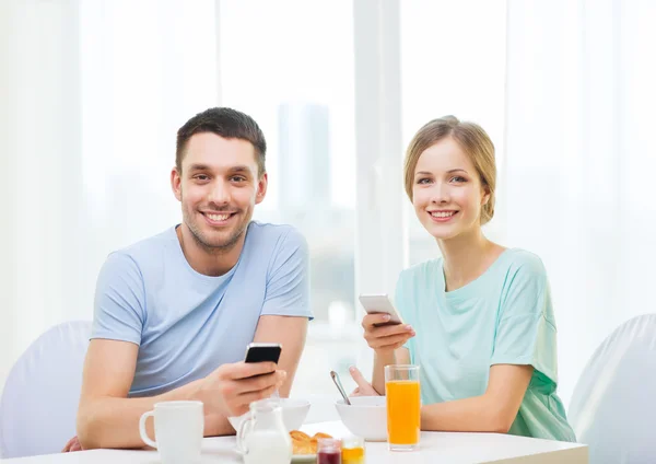 Casal sorridente com smartphones lendo notícias — Fotografia de Stock