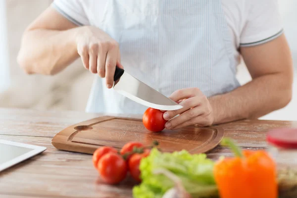 Male hand cutting tomato on board with knife — Stock Photo, Image