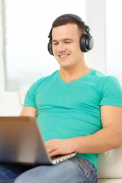 Homme souriant avec ordinateur portable et écouteurs à la maison — Photo