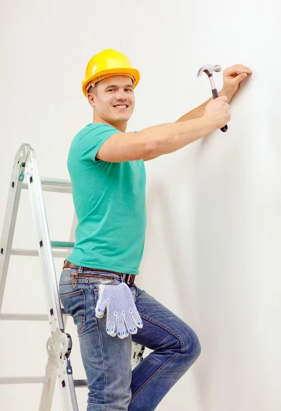 Lächelnder Mann mit Helm hämmert Nagel in Wand — Stockfoto