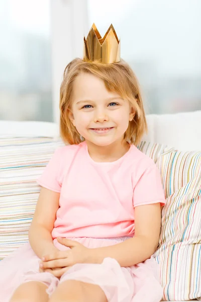 Усміхнена маленька дівчинка в короні сидить на дивані — стокове фото