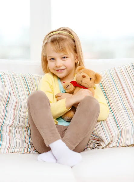 Menina sorridente com ursinho sentado no sofá — Fotografia de Stock