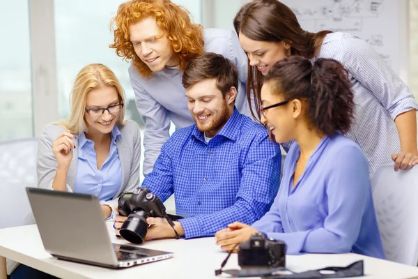 Team sorridente con laptop e fotocamera in ufficio — Foto Stock