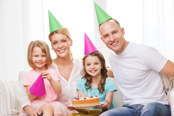 Lachende gezin met twee kinderen in hoeden met cake — Stockfoto