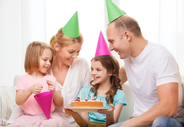 Lachende gezin met twee kinderen in hoeden met cake — Stockfoto