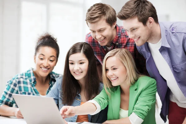 Lachende studenten kijken naar laptop op school — Stockfoto