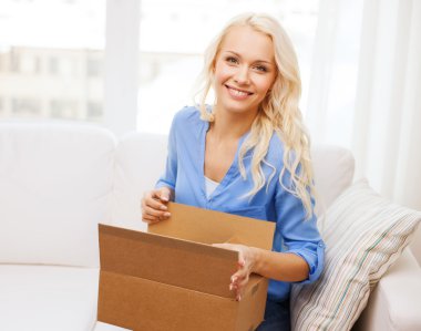 Smiling young woman opening cardboard box at home clipart
