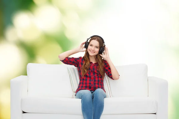 Tonårig flicka sitter på soffan med hörlurar — Stockfoto