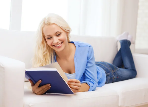 Mujer sonriente leyendo libro y acostada en el sofá —  Fotos de Stock