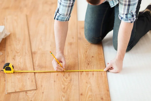 Close-up de mãos masculinas medindo piso de madeira — Fotografia de Stock