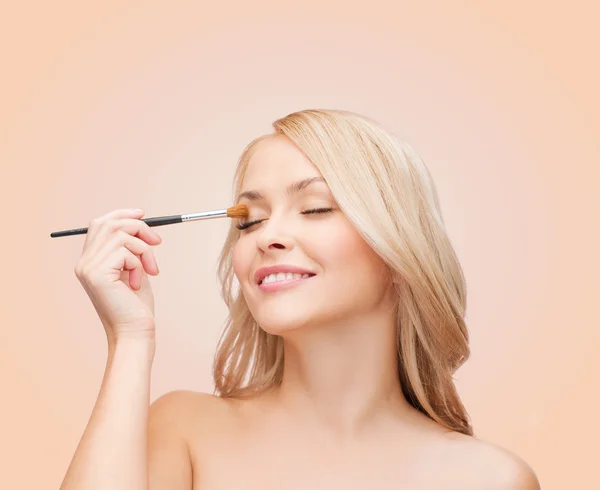 Mooie vrouw met gesloten ogen en make-up borstel — Stockfoto