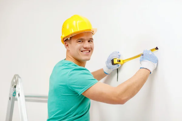 Smiling man in protective helmet measuring wall — Stock Photo, Image