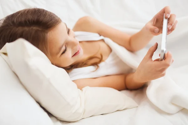 Kleines Mädchen liegt mit Smartphone zu Hause im Bett — Stockfoto