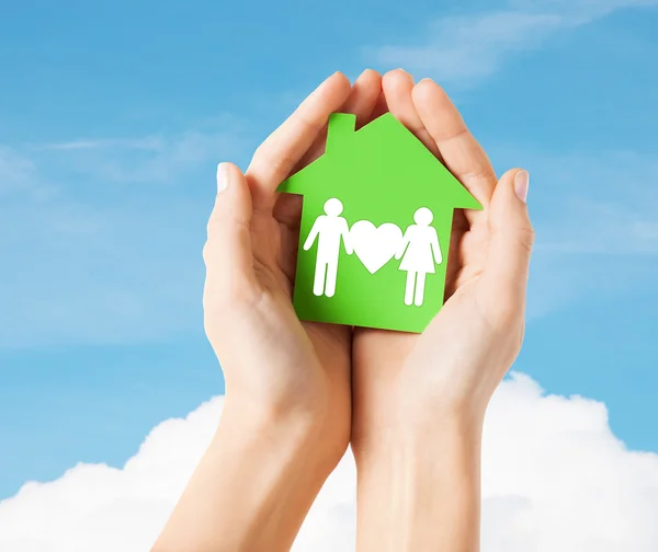 Руки держат зеленый дом с семьей — стоковое фото