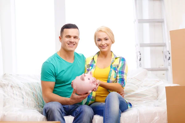 Lächelndes Paar mit Sparschwein im neuen Zuhause — Stockfoto