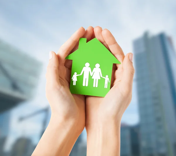 Руки тримають зелений будинок з сім'єю — стокове фото