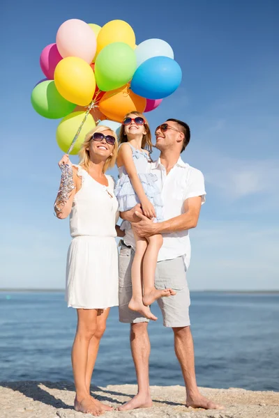 Glückliche Familie mit bunten Luftballons am Meer — Stockfoto