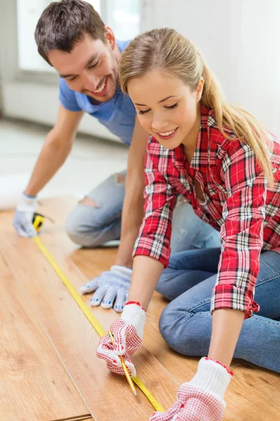 Coppia sorridente misurazione pavimenti in legno — Foto Stock