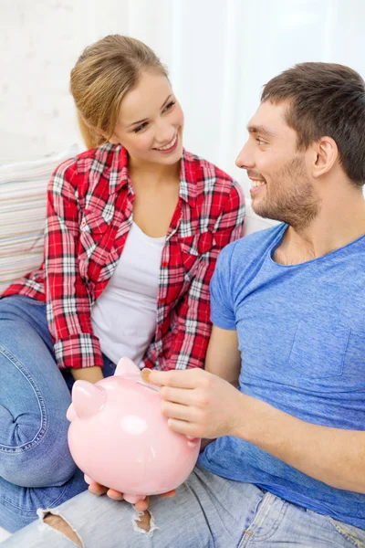 Smiling couple with piggybank sitting on sofa — Stock Photo, Image