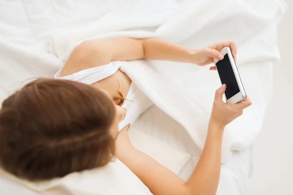 Маленька дівчинка лежить в ліжку зі смартфоном вдома — стокове фото