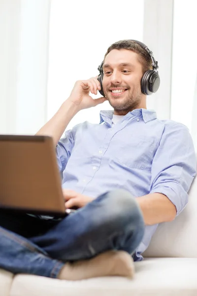 Hombre sonriente con portátil y auriculares en casa — Foto de Stock