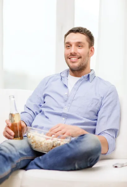 Glimlachende man met bier en popcorn thuis — Stockfoto