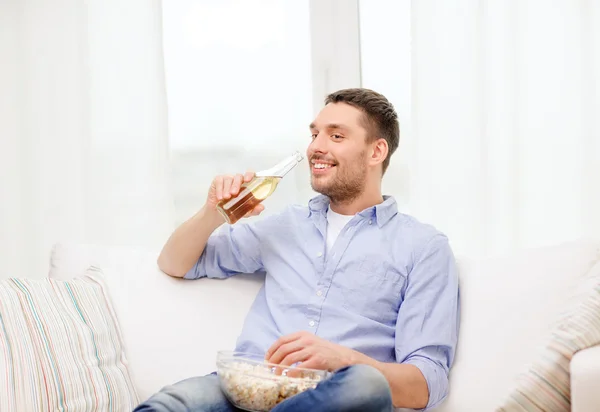 Hombre sonriente con cerveza y palomitas de maíz en casa —  Fotos de Stock