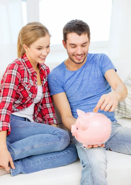 Smiling couple with piggybank sitting on sofa — Stock Photo, Image