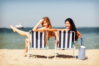 Girls sunbathing on the beach chairs clipart