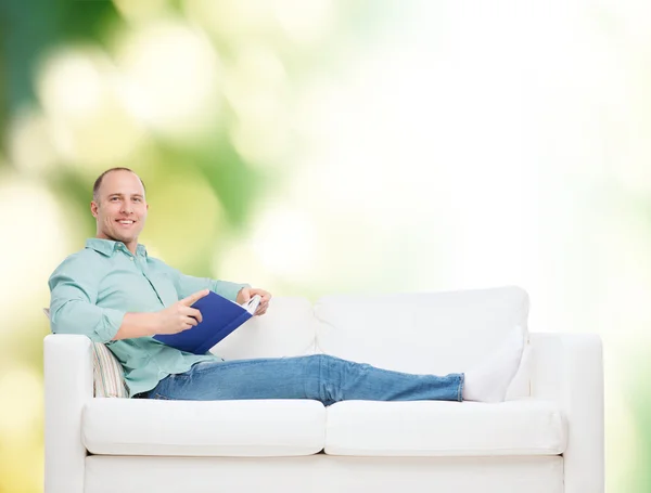 Lächelnder Mann mit Buch auf Sofa liegend — Stockfoto