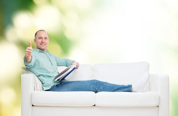 Homme souriant couché sur un canapé avec un livre — Photo