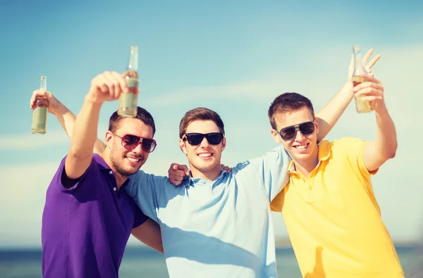 Vänner på stranden med flaskor av dryck — Stockfoto