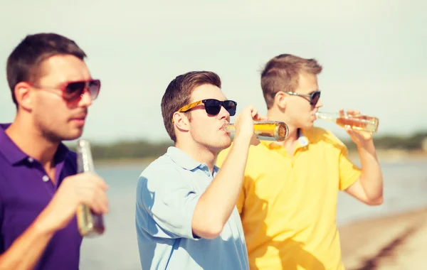 Vänner på stranden med flaskor av dryck — Stockfoto