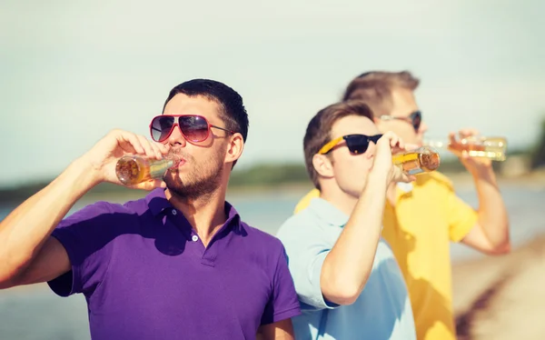 Vänner på stranden med flaskor av dryck — Stockfoto