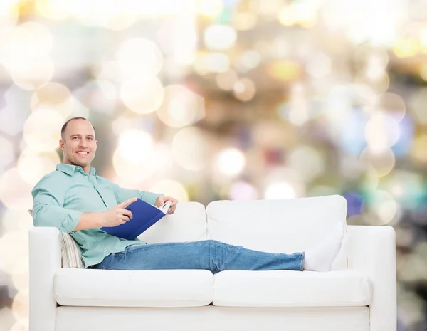 Uomo sorridente sdraiato sul divano con libro — Foto Stock