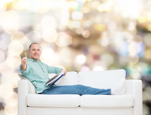 Hombre sonriente acostado en un sofá con libro —  Fotos de Stock