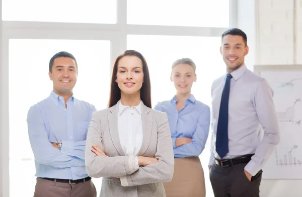 Smiling businesswoman in office with team on back — Stock Photo, Image
