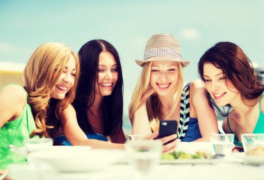 Girls looking at smartphone in cafe on the beach clipart