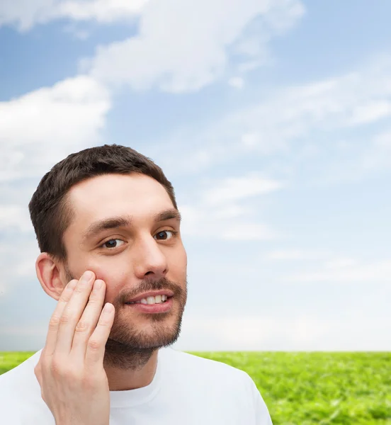 Mooie lachende man aan zijn gezicht te raken — Stockfoto