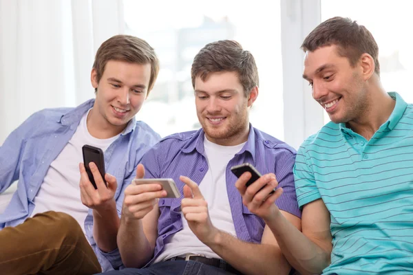 Amigos sonrientes con teléfonos inteligentes en casa — Foto de Stock