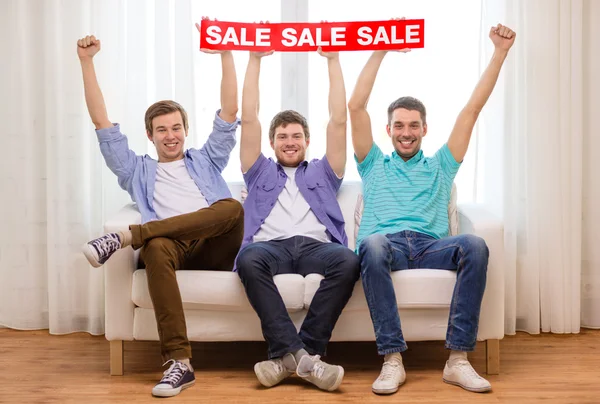 Sonrientes amigos masculinos sosteniendo venta signo — Foto de Stock