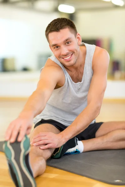 Glimlachende man die zich uitstrekt op mat in de sportschool — Stockfoto