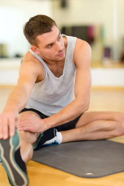 Hombre serio estiramiento en la estera en el gimnasio —  Fotos de Stock