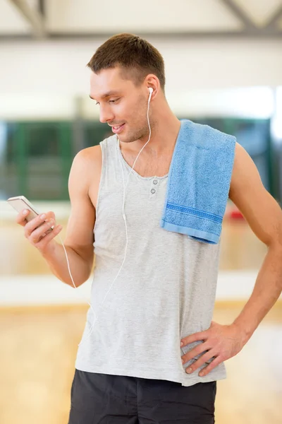 Молодой человек со смартфоном и полотенцем в тренажерном зале — стоковое фото