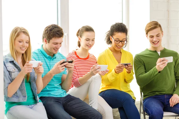 Smiling students with smartphone texting at school — Stock Photo, Image