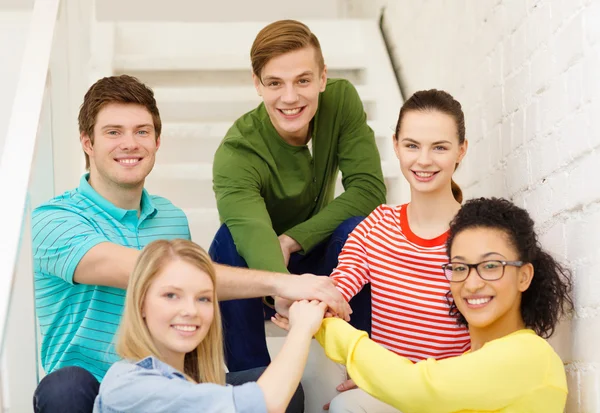 Estudantes sorridentes com as mãos em cima uns dos outros — Fotografia de Stock