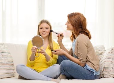 two smiling teenage girls applying make up at home